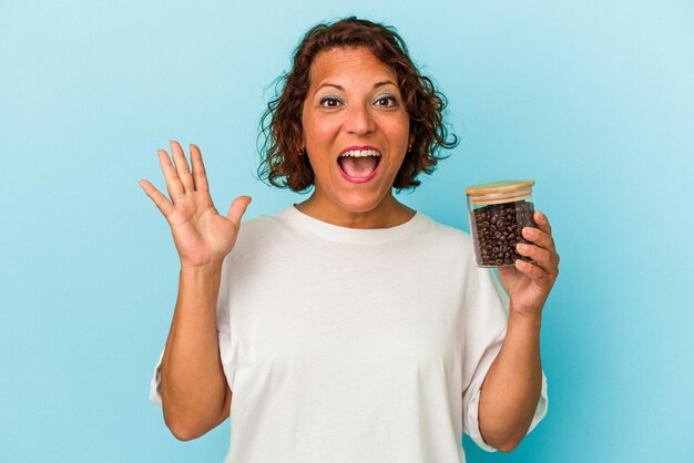 Mulher latina de meia-idade segurando uma jarra de café isolada sobre fundo azul surpresa e chocada.