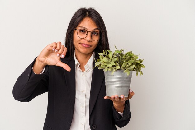 Mulher latina de negócios jovem segurando plantas isoladas no fundo branco, mostrando um gesto de antipatia, polegares para baixo. Conceito de desacordo.