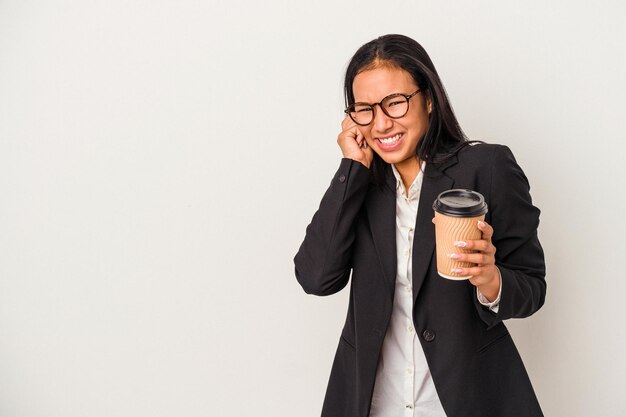 Mulher latina de negócios jovem segurando um café para viagem isolado no fundo branco, cobrindo os ouvidos com as mãos