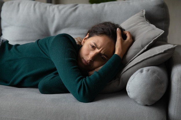 Mulher latina do milênio chateada deitada no sofá em casa se sente deprimida com problemas de vida problemas infelizes jovens hispânicas descansam no sofá angustiadas com aborto ou aborto espontâneo conceito de drama