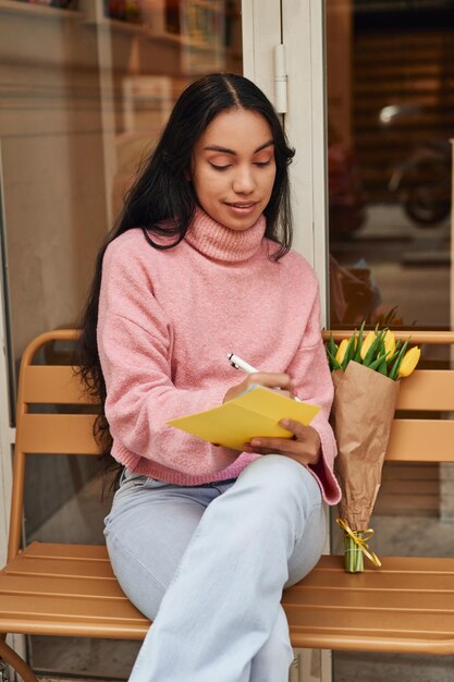 Mulher latina escrevendo carta de amor com tulipas amarelas