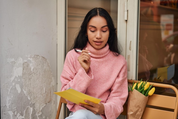 Mulher latina escrevendo carta de amor com tulipas amarelas