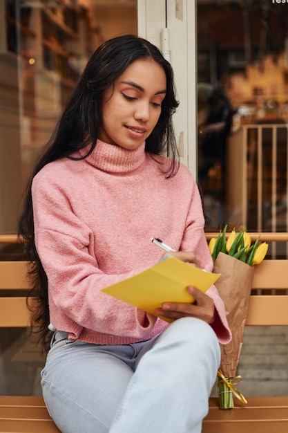 Mulher latina escrevendo carta de amor com tulipas amarelas