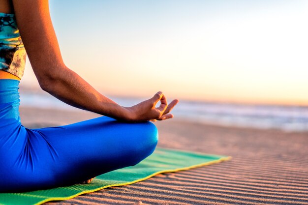 Mulher latina fazendo exercícios de ioga ou meditação ao pôr do sol na vista da praia de perto