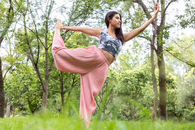 Mulher latina fazendo yogaasanas com posturas diferentes no parque ao ar livre com grama e árvores