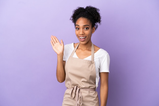 Mulher latina garçom de restaurante isolada em fundo roxo saudando com a mão com expressão feliz