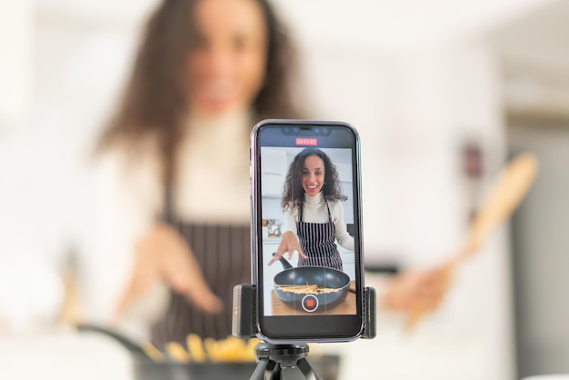 Mulher latina gravando vídeo e cozinhando na cozinha para compartilhar no blog