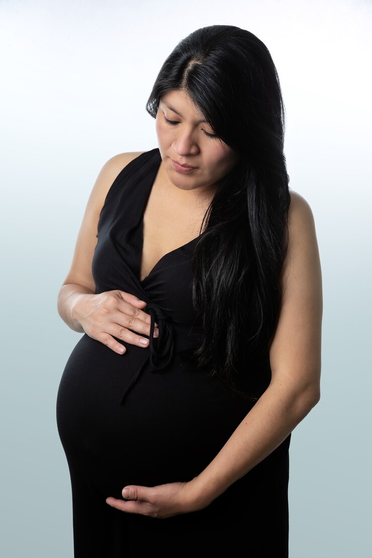 Mulher latina grávida de vestido preto segurando a barriga