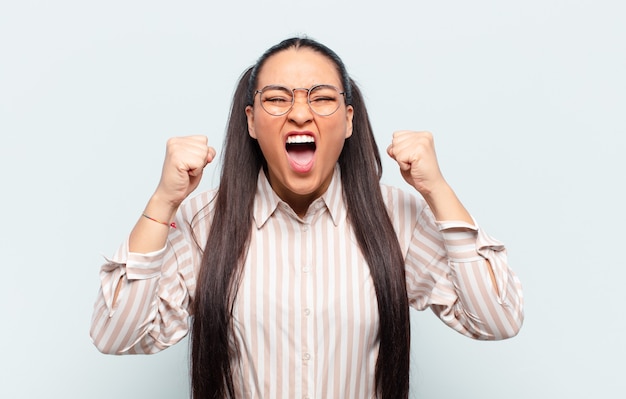 Mulher latina gritando agressivamente com uma expressão de raiva ou com os punhos cerrados celebrando o sucesso