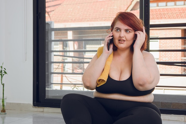 Foto mulher latina jovem plus size sentada falando ao telefone antes de começar a fazer ioga