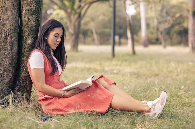 Mulher latina lendo um livro ornamentado de uma árvore no parque