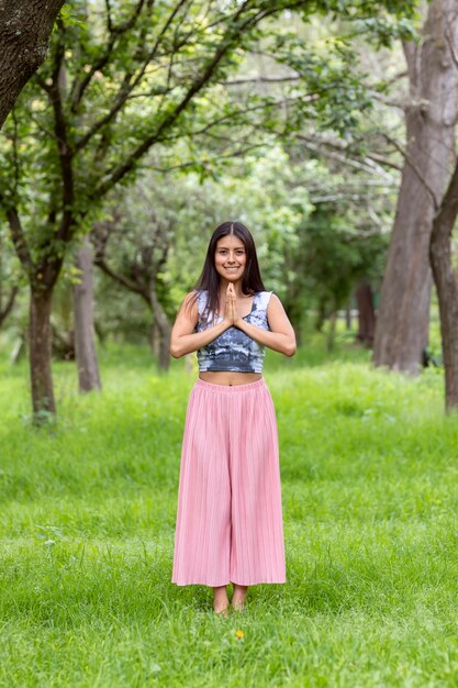 Mulher latina meditando ao lado de uma árvore no parque, na grama verde, com uma roupa rosa