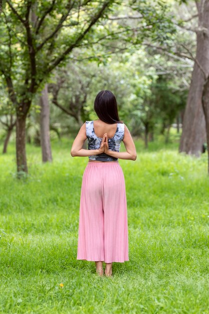 Mulher latina meditando ao lado de uma árvore no parque, na grama verde, com uma roupa rosa