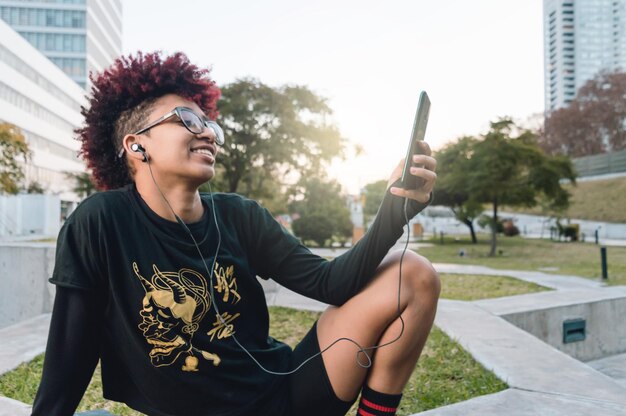 Mulher latina morena sentada sorrindo relaxada no parque assistindo redes sociais no telefone