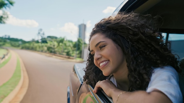 Mulher latina na janela do carro. Viagem de carro. Cabelos cacheados ao vento. Garota olha pela janela do carro.