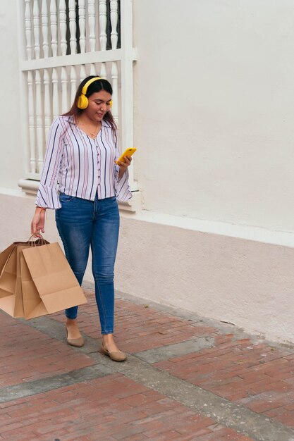 Foto mulher latina ouvindo música com fones de ouvido em pé na rua da cidade