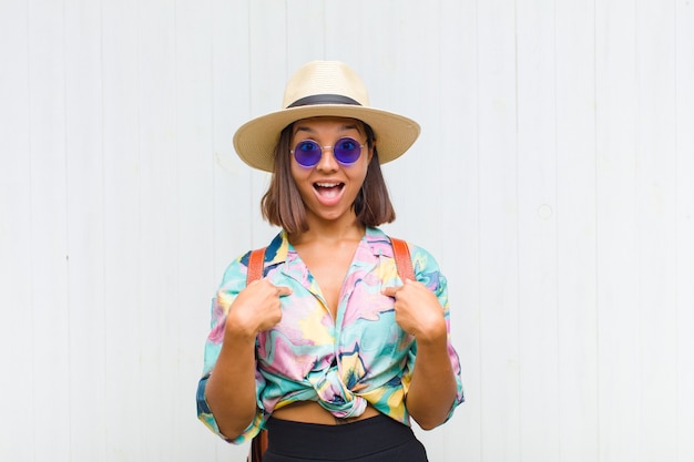 Mulher latina se sentindo feliz, surpresa e orgulhosa, apontando para si mesma com um olhar animado e surpreso