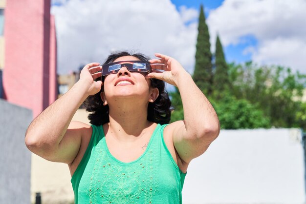 Foto mulher latina sorridente assistindo a um eclipse de sol com óculos de eclipse