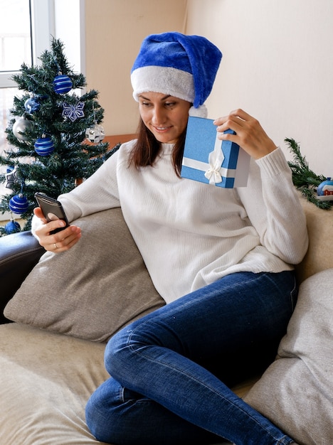 Mulher latina sorridente com chapéu de Papai Noel segurando uma caixa de presente de Natal