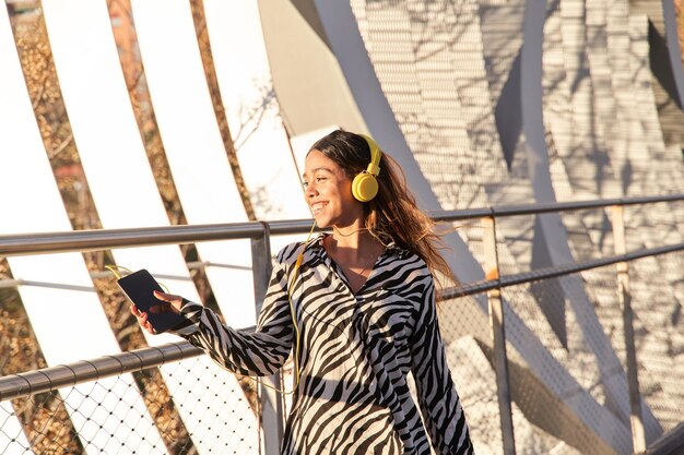 mulher latina sorridente ouvindo música com um fone de ouvido em um dia ensolarado na cidade