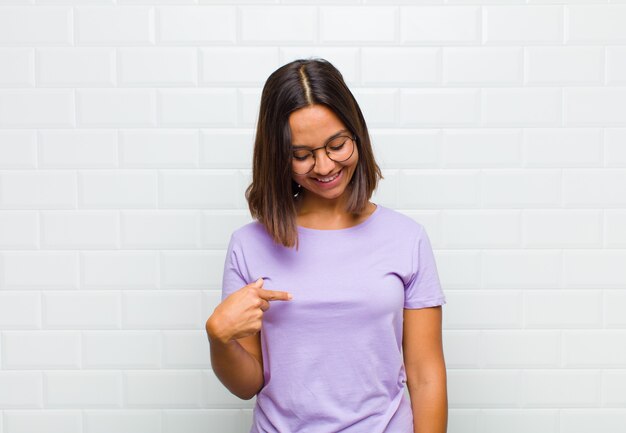 Mulher latina sorrindo alegre e casualmente, olhando para baixo e apontando para o peito