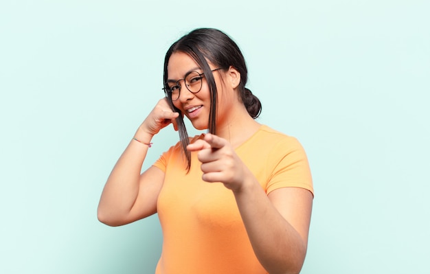 Foto mulher latina sorrindo alegremente e apontando para a câmera enquanto faz um gesto depois de ligar para você, falando ao telefone