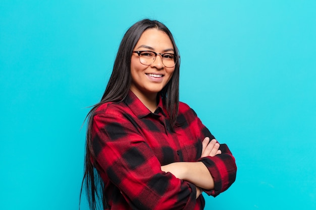 Mulher latina sorrindo com os braços cruzados e uma expressão feliz, confiante e satisfeita, vista lateral