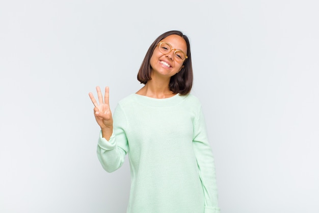 Mulher latina sorrindo e parecendo amigável, mostrando o número três ou terceiro com a mão para a frente, em contagem regressiva