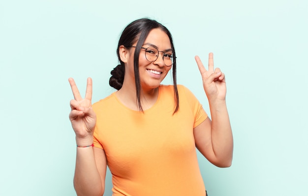 Mulher latina sorrindo e parecendo feliz, amigável e satisfeita, gesticulando vitória ou paz com as duas mãos