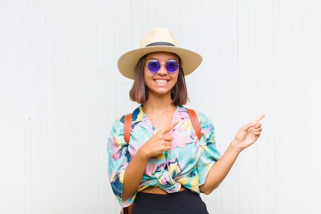 Mulher latina sorrindo feliz e apontando para o lado e para cima com as duas mãos mostrando o objeto no espaço da cópia