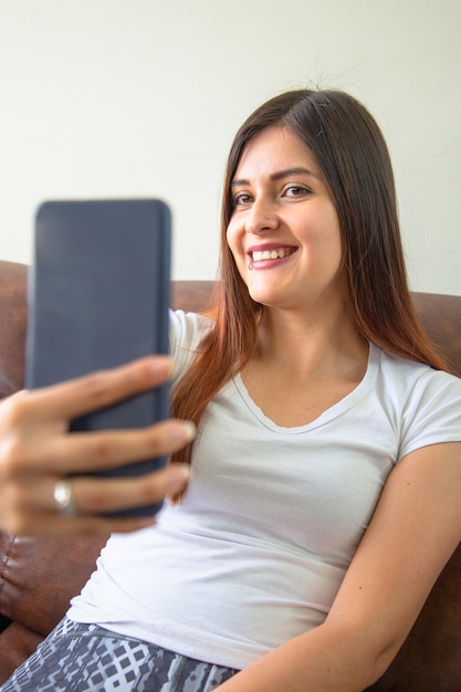 Mulher latina tomando uma selfie no sofá em sua casa