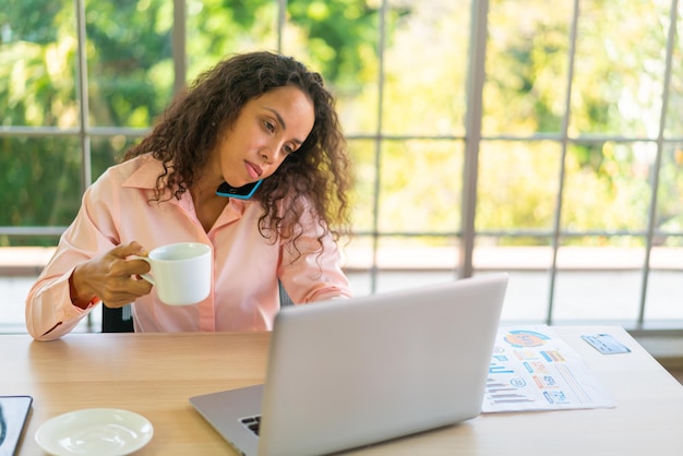 Mulher latina trabalhando com uma xícara de café na área de trabalho em casa