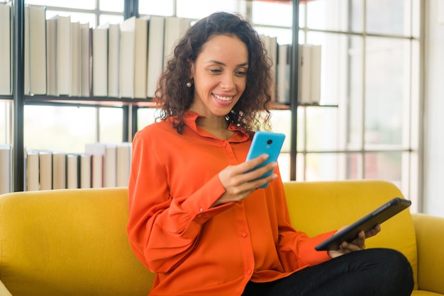 Mulher latina usando telefone celular ou smartphone e segurando o tablet em casa