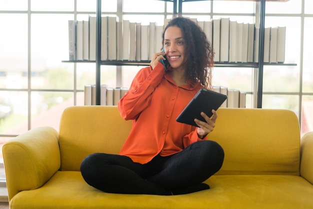 Mulher latina usando telefone celular ou smartphone e segurando o tablet em casa