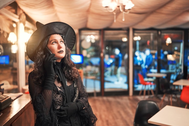Mulher latina vestida de bruxa em um café ou restaurante falando no celular