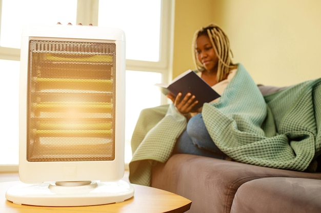 Mulher latino-americana com cobertor lendo um livro em sala fria com aquecedor