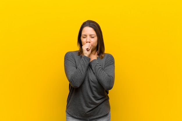 Mulher latino-americana que se sente doente com sintomas de dor de garganta e gripe, tosse com a boca coberta isolada