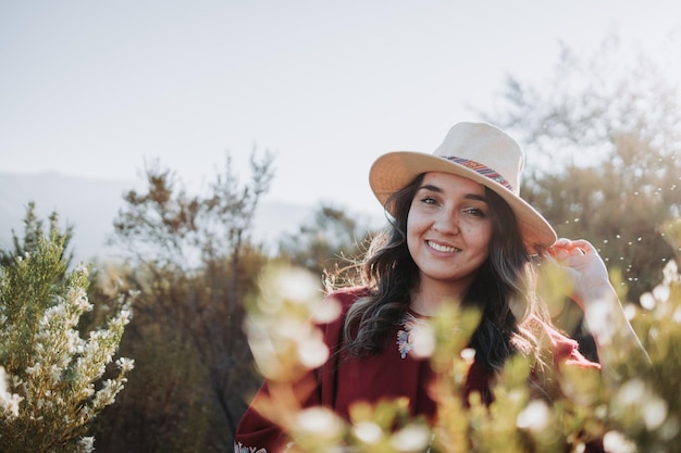 Mulher latino-americana tradicional vestindo um poncho vermelho e um chapéu visto de trás em um espaço natural