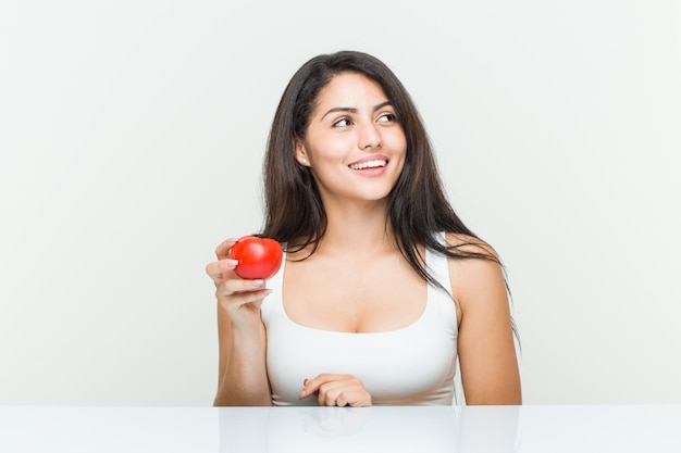 Mulher latino-americano nova que mantém um sorriso do tomate seguro com braços cruzados.