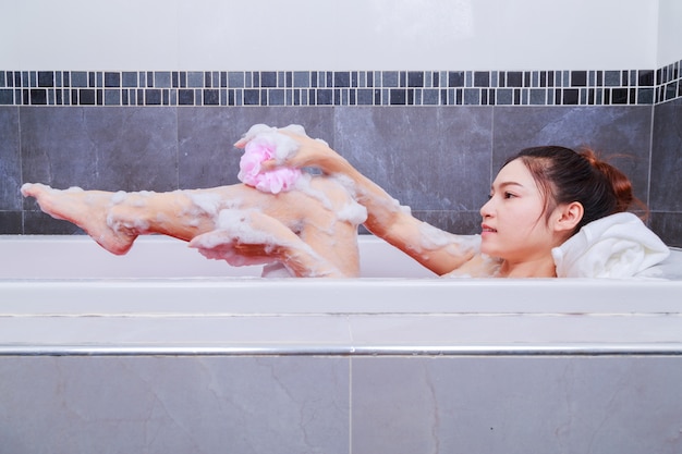 Mulher lavando a perna com esponja rosa