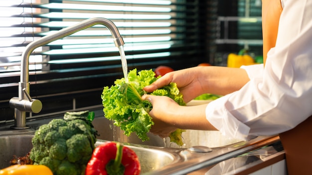 Mulher lavando legumes para preparação de salada vegana