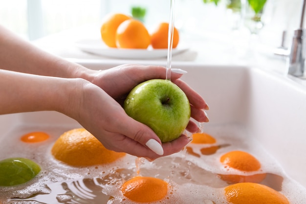 Foto mulher, lavando, maçã, torneira, em, a, pia, cozinha, embeber, frutas, em, água sabão, completamente, lava