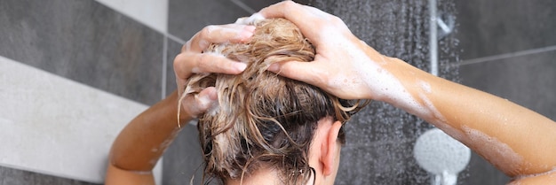 Mulher lavando o cabelo com shampoo na vista traseira do chuveiro