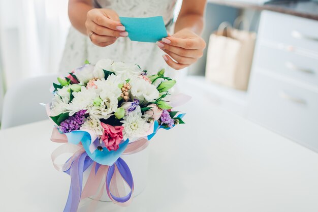 Mulher lê cartão deixado no buquê de flores pelo namorado na caixa de presente na cozinha em casa. presente surpresa