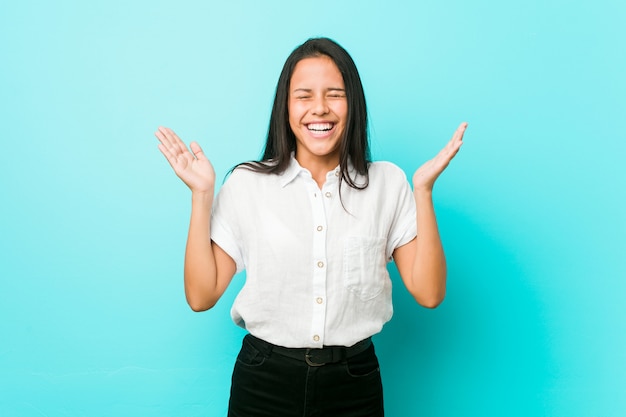 Mulher legal latino-americano nova contra uma parede azul alegre que ri muito. Conceito de felicidade.