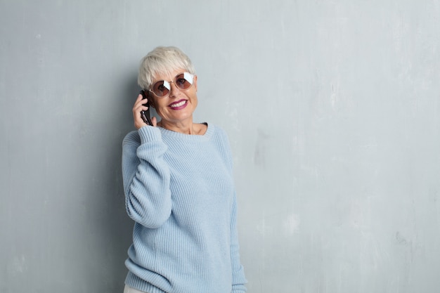 Mulher legal sênior com um telefone inteligente contra parede de cimento grunge