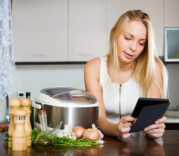 Mulher lendo ereader e cozinhando com crockpot