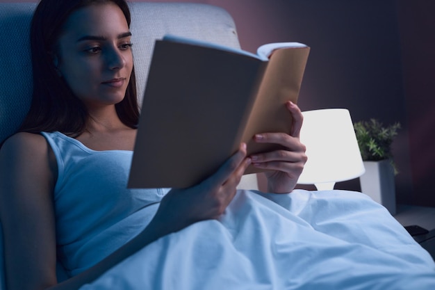 Mulher lendo livro na cama antes de dormir