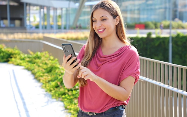 Mulher lendo mensagens no aplicativo do smartphone para bater um papo na rua da cidade