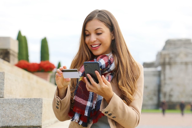 Mulher lendo o número do cartão de crédito enquanto faz compras online com o smartphone